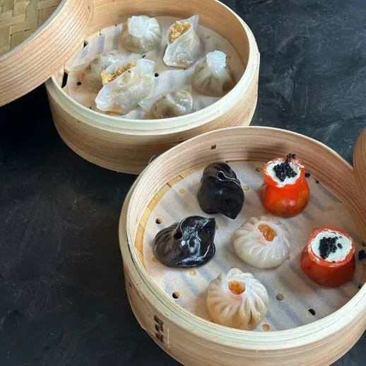 Разнообразные паровые пельмени и димсам в деревянных пароварках на черном фоне