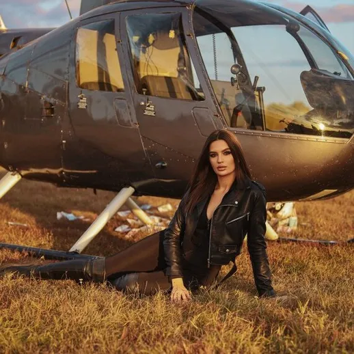 Молодая женщина в кожаной куртке позирует возле вертолета на закате