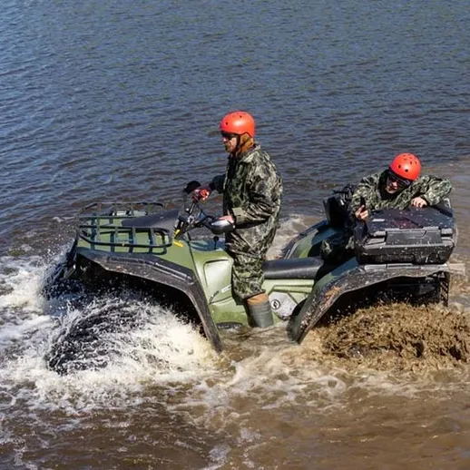 Квадроцикл пересекает реку с двумя пассажирами в спортивной экипировке под ярким небом