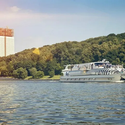 Корабль плывет по реке в Москве, наслаждаясь солнечным днем и зелеными холмами на берегу