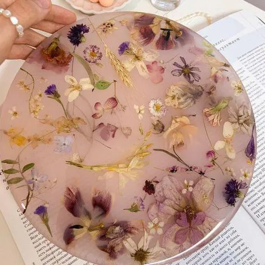 Цветочная тарелка с засушенными цветами на столе, окруженная страницами книги и аксессуарами на фоне уютного интерьера
