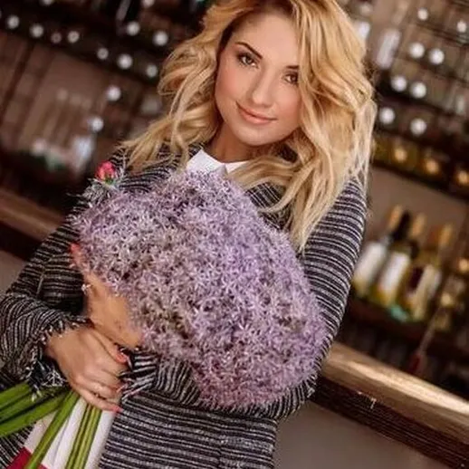 Молодая женщина с букетом светло-фиолетовых цветов на фоне стильного бара в вечернее время