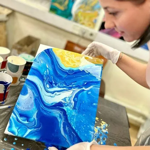 Женщина создает абстрактную картину с использованием техники акрилового литья в художественной студии