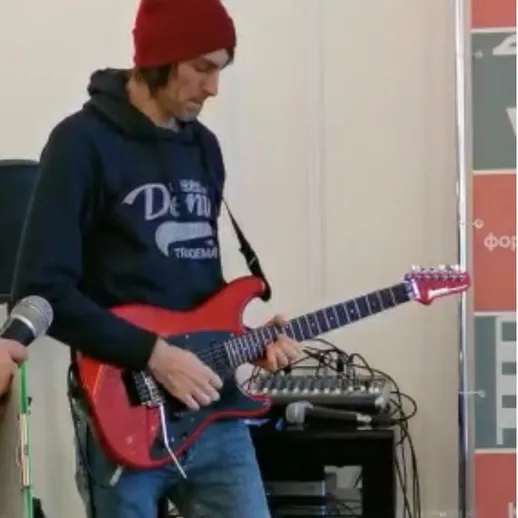Музыкант в красной шапке играет на электрогитаре во время репетиции в помещении
