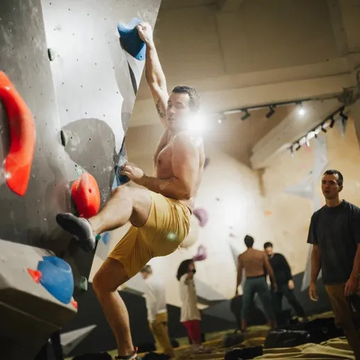 Молодой человек занимается скалолазанием в закрытом зале с искусственными стенами в вечернее время