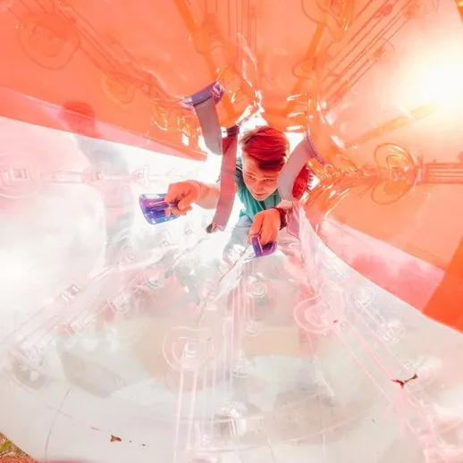 Мальчик играет в прозрачном надувном шаре на открытом воздухе в парке с яркими окружениями