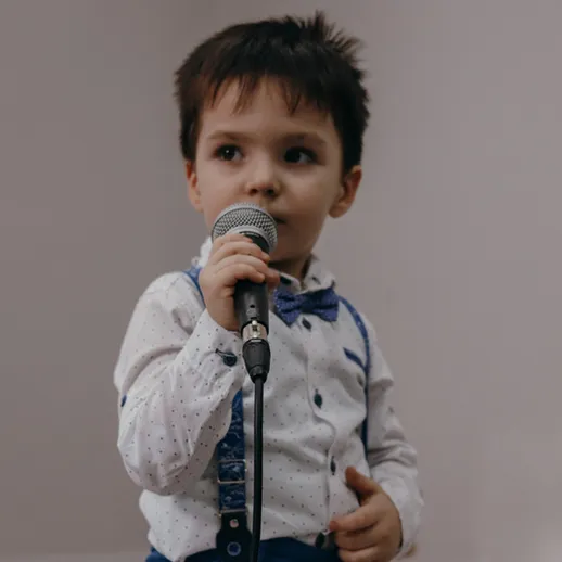 Мальчик с микрофоном выступает на сцене на детском празднике в уютном зале