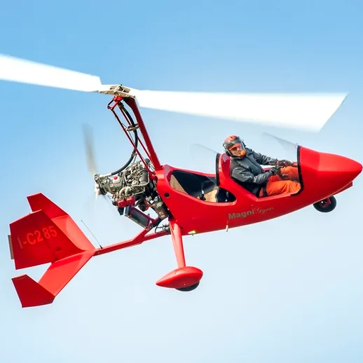 Летчик управляет красным автожиром в ясном небе над живописным ландшафтом в солнечный день