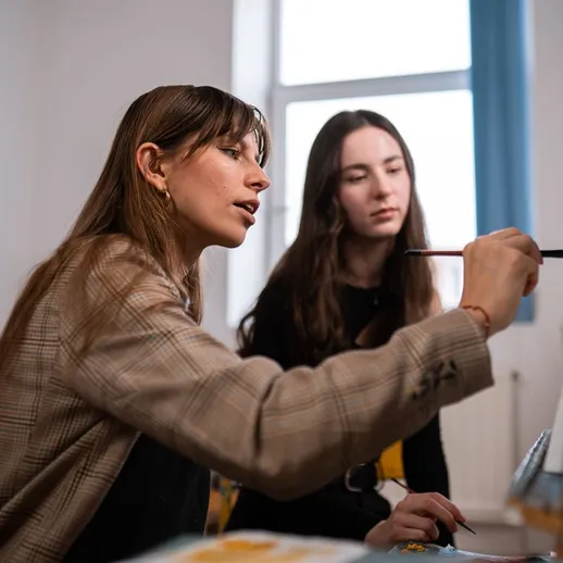 Урок рисования в уютной студии, где преподаватель обучает ученицу живописи на фоне окна