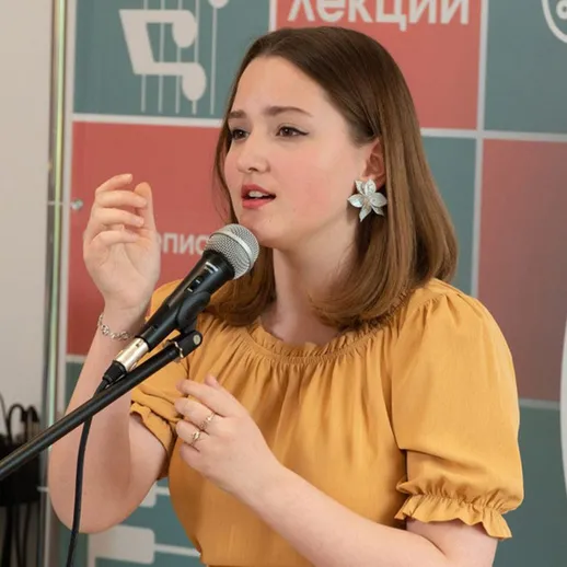 Молодая женщина выступает на сцене на лекции, делая акцент на важные моменты во время мероприятия