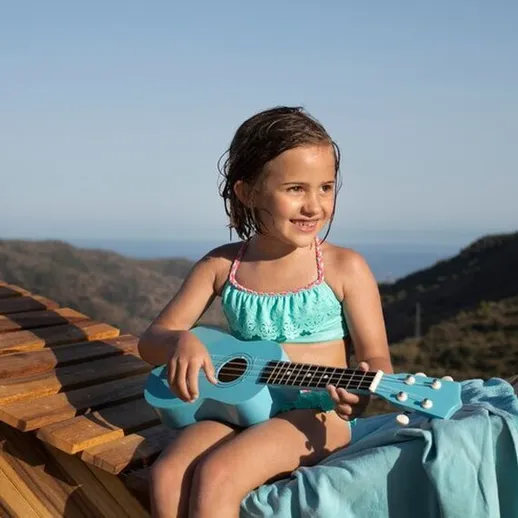 Девочка в купальнике играет на укулеле на террасе с видом на море