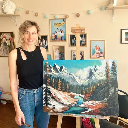 Художница представляет свою работу в мастерской с картинами пейзажей гор