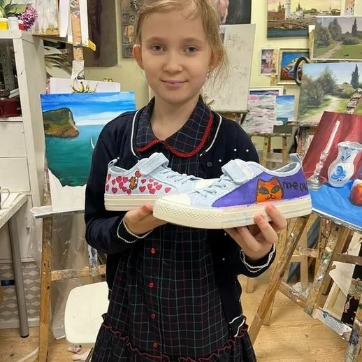 Девочка показывает кастомизированные кроссовки в художественной мастерской во время урока рисования