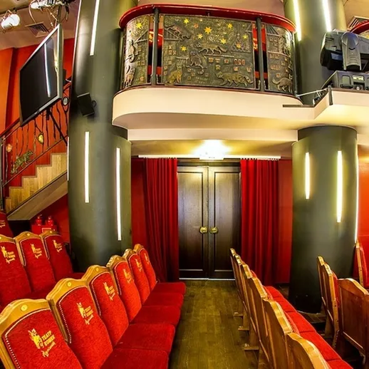 Уютный зал театра с красными мягкими креслами и сценой, готовый к представлению в вечернее время