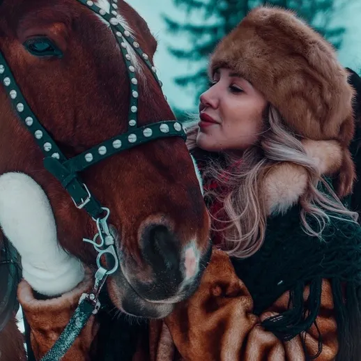 Девушка в шубе обнимает коня на зимней прогулке в лесу