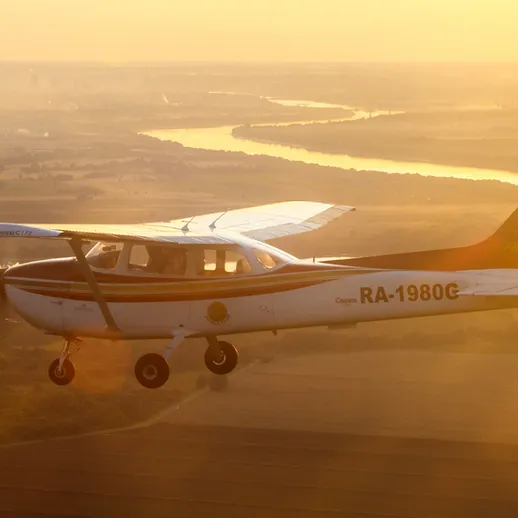 Полет легкого самолета над живописным природным ландшафтом во время заката