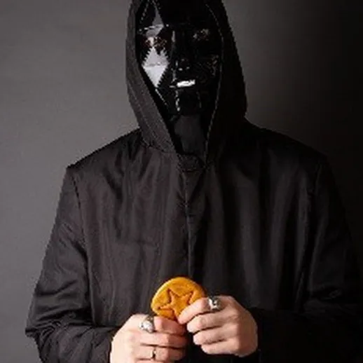 Человек в черной маске держит загадочный предмет на фоне однотонной поверхности в темном освещении