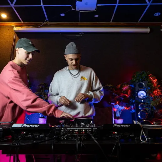 Два диджея работают за пультами в студии звукозаписи с эффектным освещением