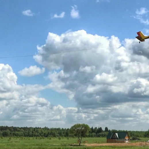 Самолёт тянет дельтаплан над зеленым лугом в солнечную погоду на фоне облачного неба