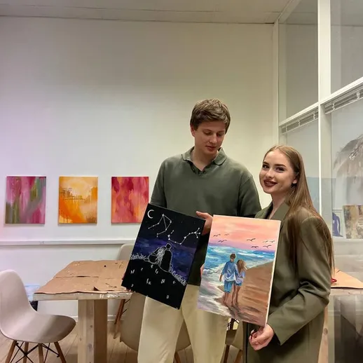 Молодая пара с картинами в художественной студии на фоне работ других художников