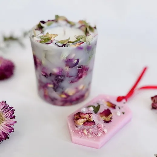 Ароматная свеча с лепестками цветов и декоративный аксессуар, украшенный розами, на белом фоне