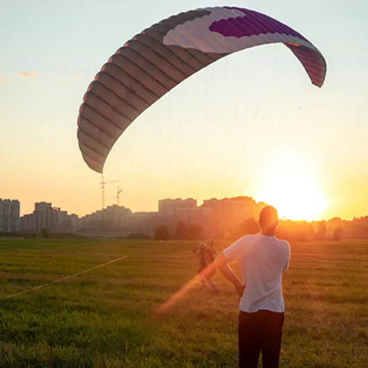 Парапланерист запускает параплан на закате в зеленом поле, создавая волшебную атмосферу