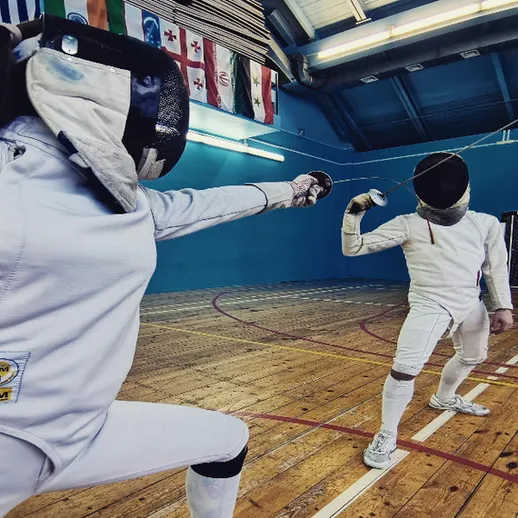 Соревнование по фехтованию в спортивном зале с участниками в защитной экипировке и фехтовальными мечами