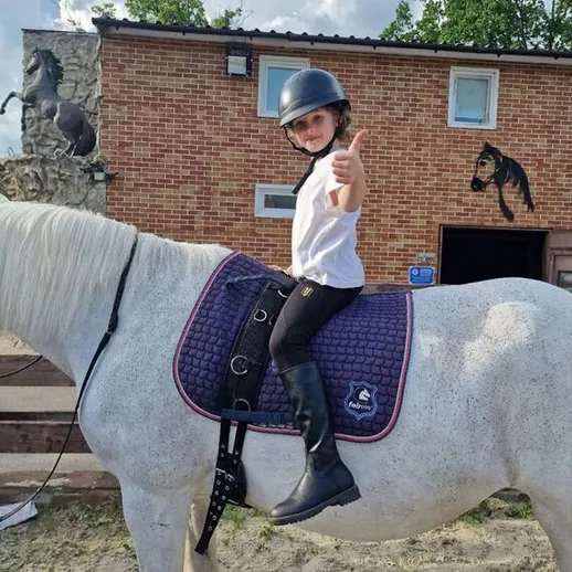 Девочка катается на лошади в конном клубе, радуясь солнечному дню
