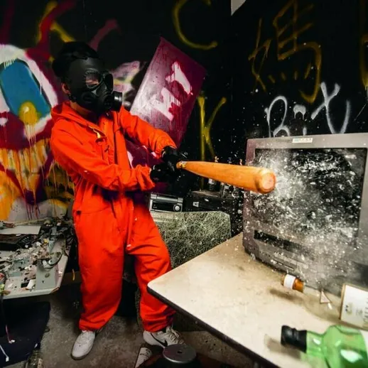 Человек в защитном костюме разбивает телевизор битой в заброшенном помещении