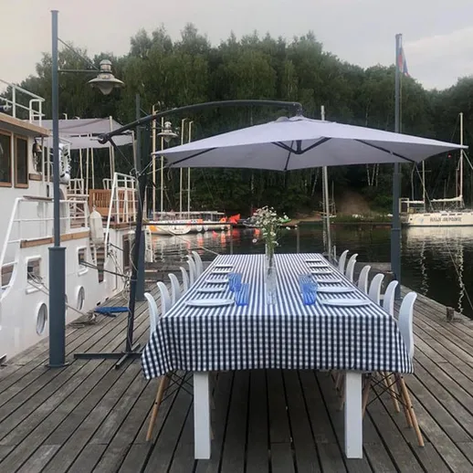 Элегантный обеденный стол на пирсе у воды с зонтами и яхтами на фоне