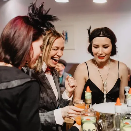 Три женщины наслаждаются коктейлями на вечеринке в стильном интерьере, вечерняя одежда и улыбки создают атмосферу праздника