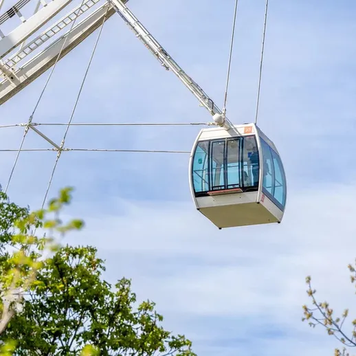 Кабина колеса обозрения на фоне голубого неба и зелёных деревьев в парке
