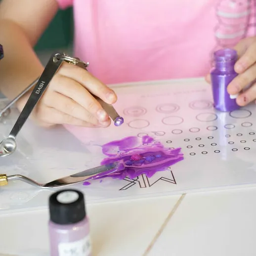 Детская рука наносит фиолетовую краску на прозрачный шаблон в творческой мастерской