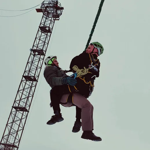 Мужчина и женщина на веревке спускаются с высоты на фоне строительной крана в холодный зимний день