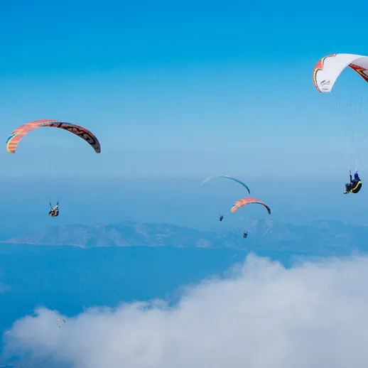 Парапланеристы наслаждаются полетом над облаками в солнечный день на высоких горных склонах