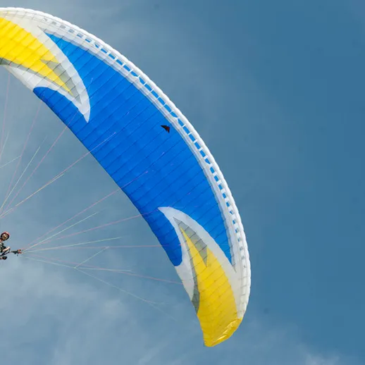 Парапланерист в ярком параплане пролетающий над живописной местностью под ясным небом в солнечный день