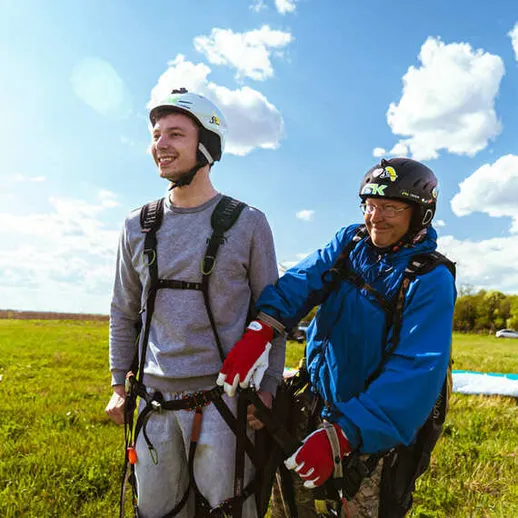 Парапланеристы готовятся к полету на зеленом поле под голубым небом с облаками в теплый солнечный день