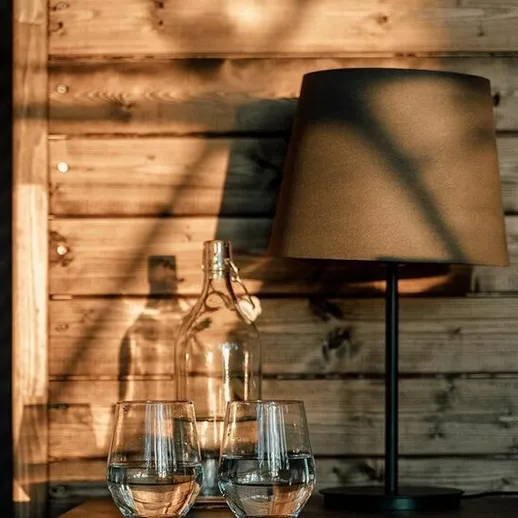 Стильный интерьер с лампой и стеклянными стаканами на деревянном столе в свете заката