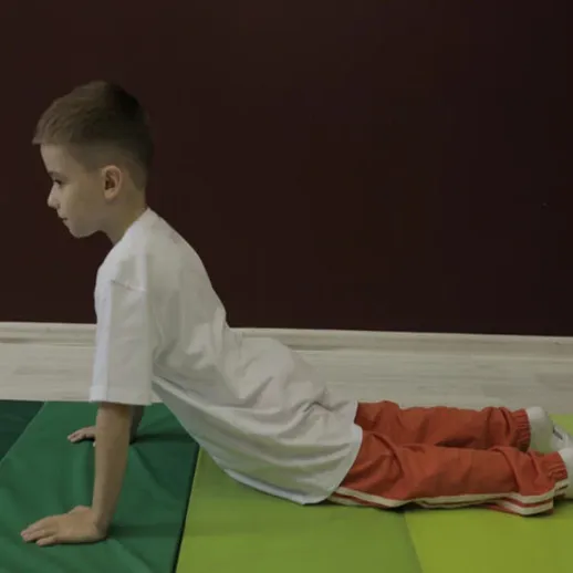 Мальчик выполняет упражнения на коврике в спортивном зале во время тренировки утром