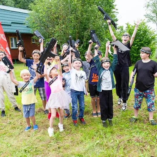 Дети и взрослые играют с игрушечным оружием на природе у загородного дома во время летнего отдыха