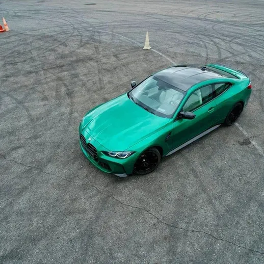 Зеленый спортивный автомобиль на подиуме, оставляющий следы на асфальте во время дрифта на автодроме