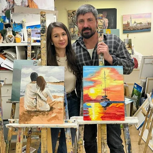 Молодая пара позирует с двумя картинами на выставке в художественной студии, находясь в творческой атмосфере