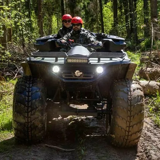 Два человека едут на квадроцикле по лесной тропе весной в солнечный день