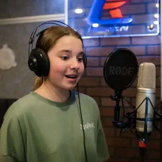 Девочка поет в студии звукозаписи с микрофоном и наушниками