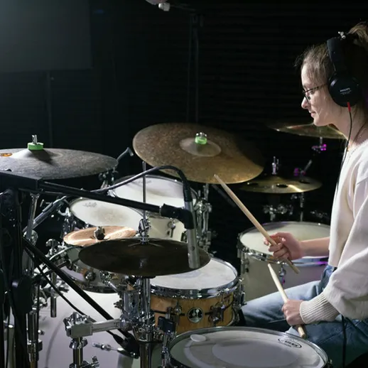 Молодая женщина играет на барабанах в студии, освещенной мягким светом, во время записи музыки