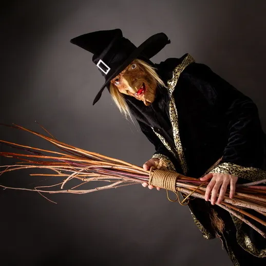 Ведьма с метлой в черном плаще на темном фоне готовится к колдовству в ночное время