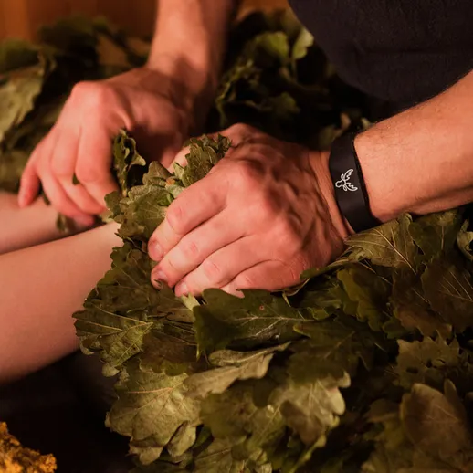 Мужчина укрывает ноги листьями на лечебной процедуре в бане в холодный сезон