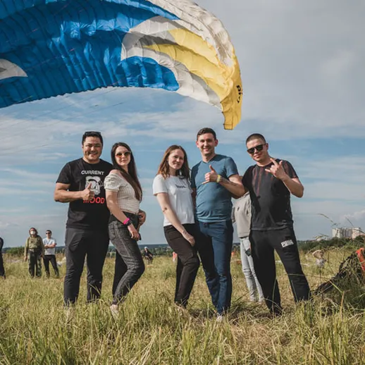 Группа друзей позирует на поле после парапланеризма в солнечный день