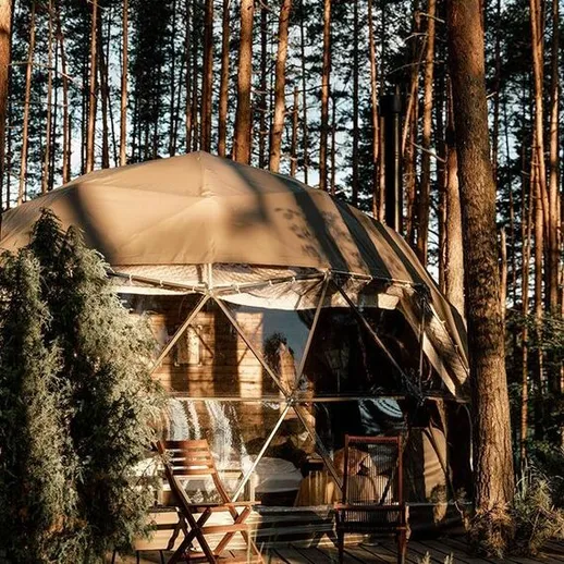 Уютная геодезическая палатка в лесу, окруженная высокими деревьями в солнечный день