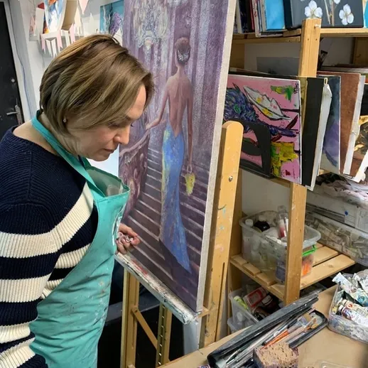 Художник работает над картиной в своей студии, окруженный творческими материалами и инструментами